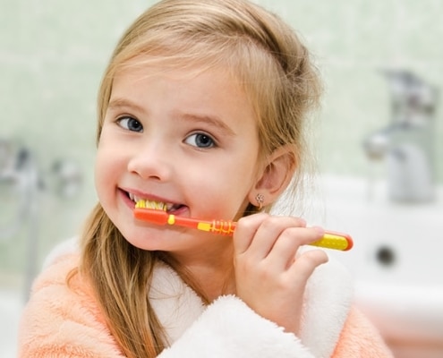 Young child smiling and brushing her teeth.